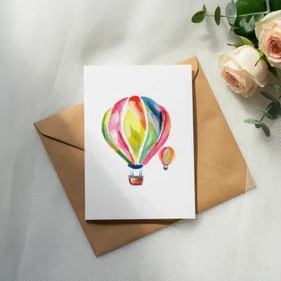 Watercolor hot air balloons on a white card atop a brown envelope.