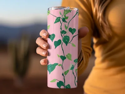 Pink tumbler with a green vine and leaf pattern held by a hand.