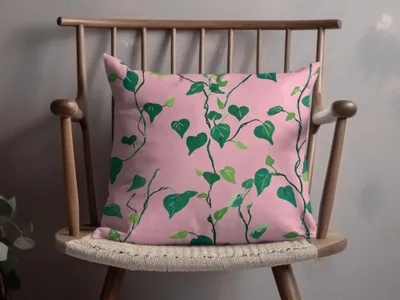 Pink throw pillow with green leafy vine pattern on a wooden chair.