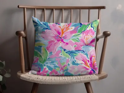 Floral throw pillow with pink hibiscus blooms on a wooden chair.