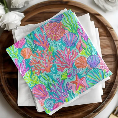 Colorful coral and seashell pattern on folded napkins, arranged on a wooden tray.