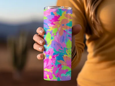 Hand holds colorful floral patterned tumbler with blurred background.