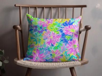 Floral throw pillow with vibrant pink, blue, and green watercolor flowers on a wooden chair.