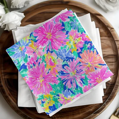 Colorful floral print napkins stacked on a wooden tray with white napkins.