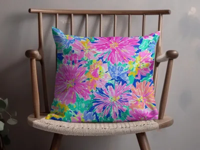 Floral throw pillow with pink, blue, and green abstract flowers on a wooden chair.