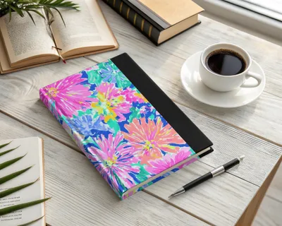 Floral patterned journal with a pen and coffee cup on a wooden desk.