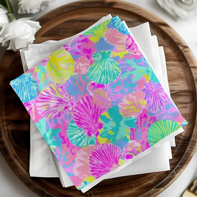 Pink, blue, and green seashell pattern on folded napkins on a wooden tray.