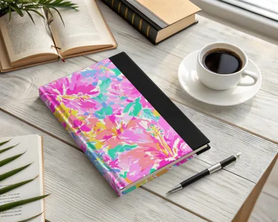 Journal with a vibrant floral cover, coffee, and pen on a wooden desk.