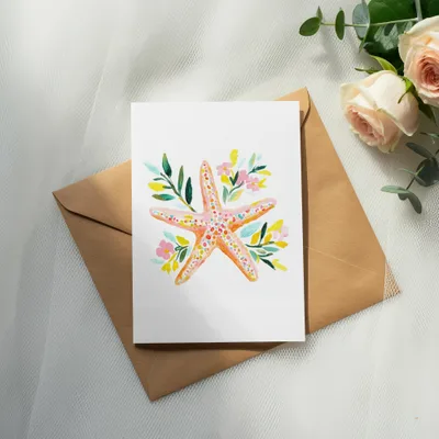 Watercolor painting of a pink starfish with flowers and leaves on a card.