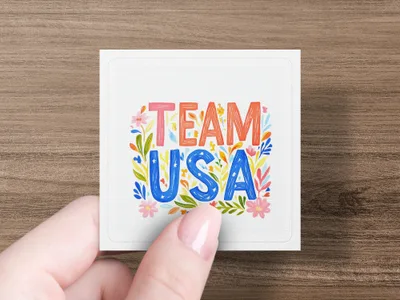 Hand holds card with colorful "TEAM USA" text and floral accents.