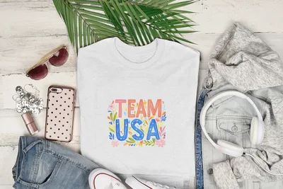 White t-shirt with "Team USA" and floral design, displayed with jeans and accessories.