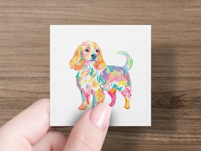Colorful watercolor dog illustration on a white square card held by a hand.