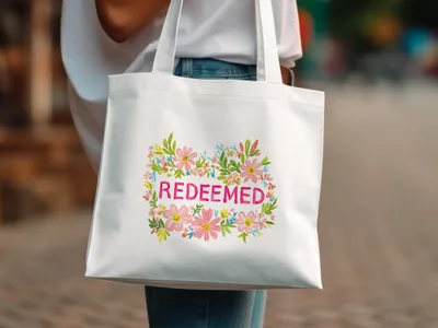 White tote bag with "Redeemed" text inside a floral wreath.