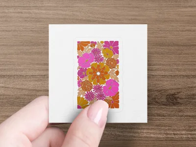 Hand holding a square sticker with a retro floral pattern in orange and pink.