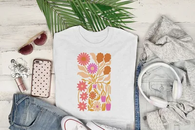 White t-shirt with a floral abstract design, surrounded by clothing and accessories.