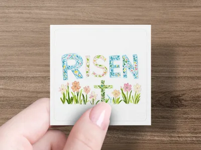 "Risen" text with floral accents and a cross on a card held by a hand.