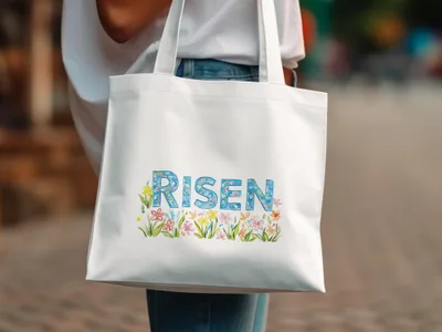 White canvas tote bag with "RISEN" text surrounded by colorful floral illustrations.