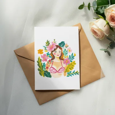 Watercolor illustration of a woman's face with flowers and foliage, on a card atop an envelope.