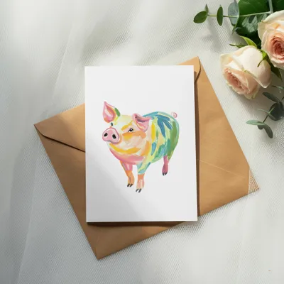 Colorful painted pig illustration on card atop envelope with roses.