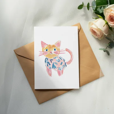 Watercolor painting of a whimsical orange cat with a blue floral shirt on a card.