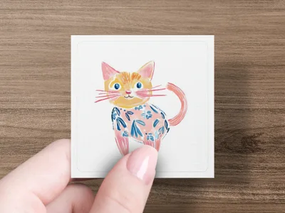 Cartoon cat with blue floral pattern on white card held by fingers.