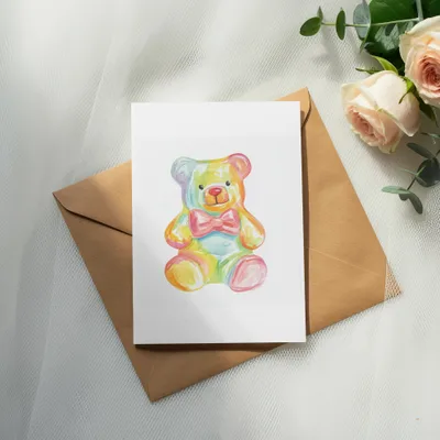 Colorful teddy bear drawing on a card atop a brown envelope.