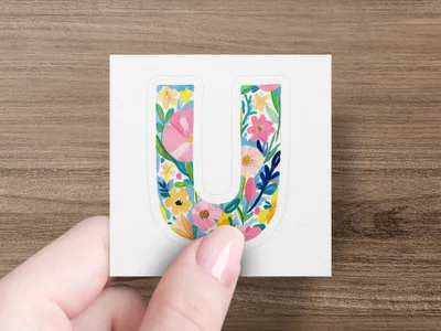 Hand holding a decorative floral letter 'U' sticker.