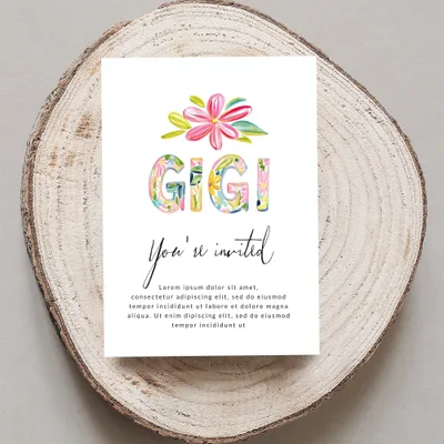 "Gigi You're invited" card with floral letters on wood slice.