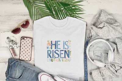 White t-shirt with "He Is Risen" text and floral design.