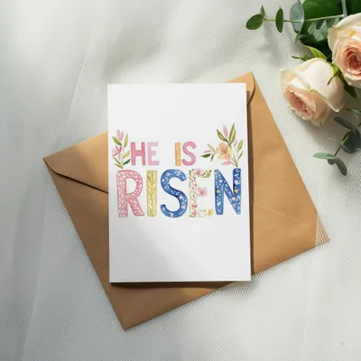 "HE IS RISEN" text on a card with floral accents, on a brown envelope.