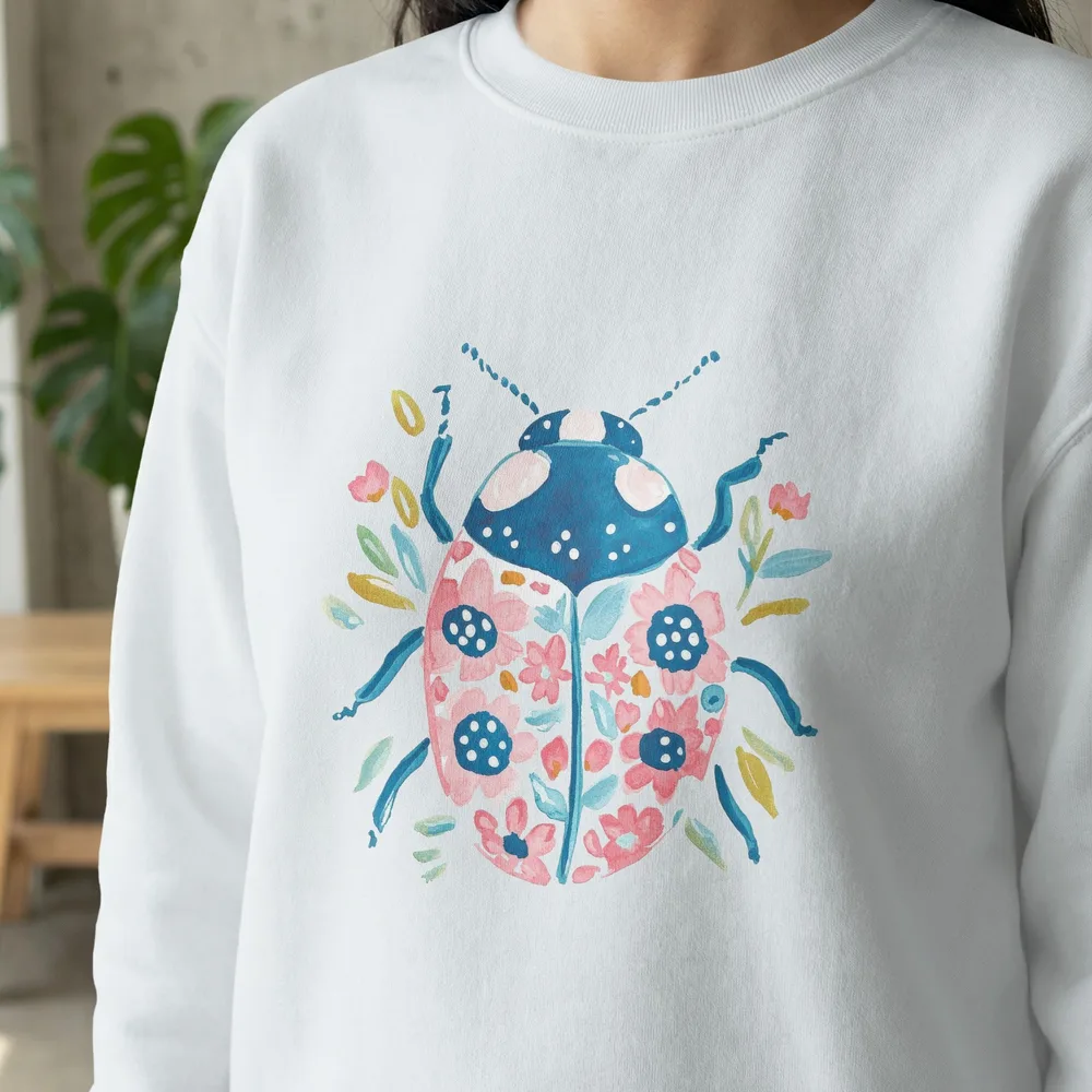 White sweatshirt with a watercolor ladybug and floral design.