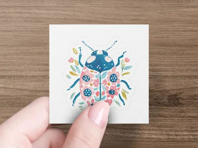 Ladybug sticker with pink floral pattern on white background held by fingers.