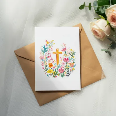 Watercolor cross with floral border on card with brown envelope.