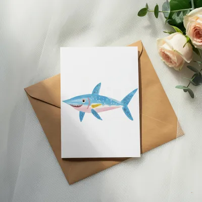 Watercolor illustration of a blue shark on a card, placed on a brown envelope.
