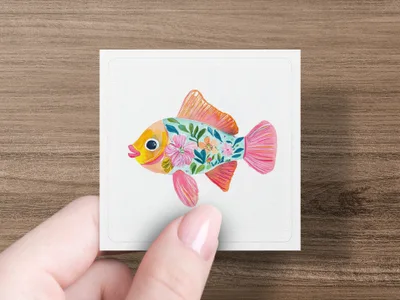 Pink fish with colorful floral patterns on white card held by fingers.