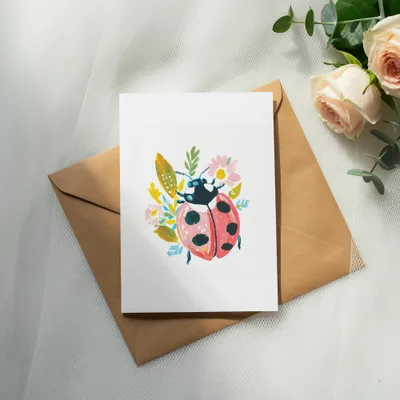 Greeting card with ladybug and floral illustration on a kraft paper envelope.