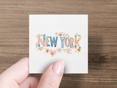 "NEW YORK" text with floral illustrations on a white sticker held by a hand.