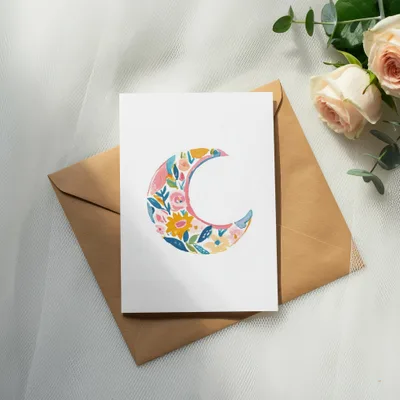 Floral crescent moon design on a white card with a brown envelope.