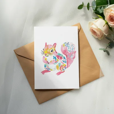 Watercolor painting of a colorful squirrel on a card, resting on an envelope.