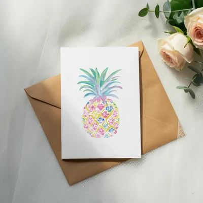 Watercolor pineapple illustration on white card with brown envelope and roses.
