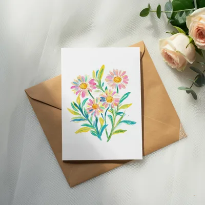 Watercolor daisies on a card laid on a brown envelope, with roses and eucalyptus.