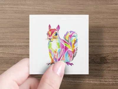 Watercolor illustration of a colorful squirrel on a white card held by a hand.