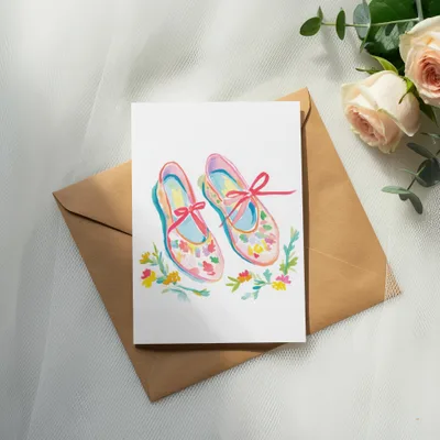 Watercolor illustration of ballet slippers with floral accents on a card.