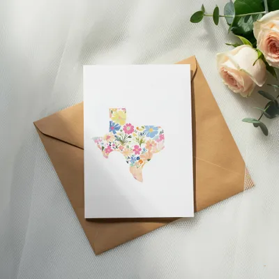Card with floral Texas outline resting on brown envelope, with roses and greenery.