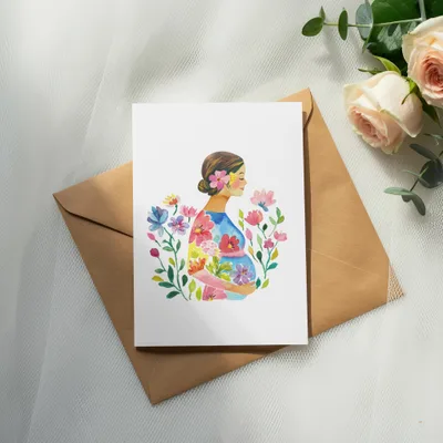 Watercolor painting of pregnant woman with flowers on a card atop an envelope.