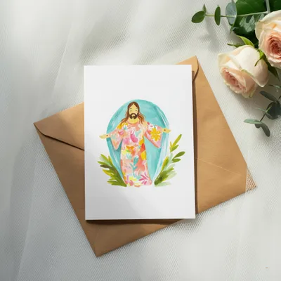 Jesus in colorful robe with open arms on a card atop envelope.