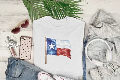 White t-shirt with Texas flag watercolor design, surrounded by casual clothing items.
