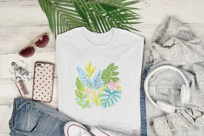 White t-shirt with colorful tropical leaf and floral design, laid flat with accessories.