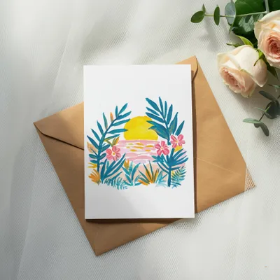 Watercolor card with sunset, palm leaves, and flowers on a kraft envelope.