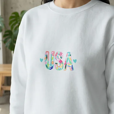White sweatshirt with "USA" in colorful floral lettering and small blue hearts.